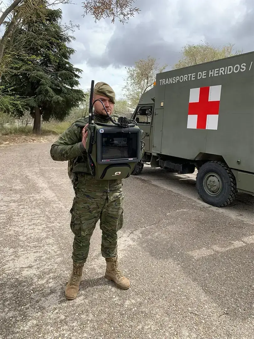 Soldier using QORE HEALTH AI-powered portable diagnostic device in the field next to a military ambulance